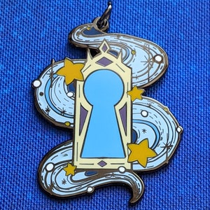 May include: A gold-toned keyhole-shaped charm with a blue keyhole and a swirling design of stars and white dots on a blue background.