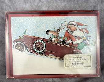 Könnte beinhalten: Eine Schachtel mit Weihnachtskarten mit dem Weihnachtsmann und einem Rentier, die in einem weinroten Oldtimer durch eine verschneite Szene fahren. Der Text auf der Karte lautet: "Santa Claus is going to town! Happy Holidays."