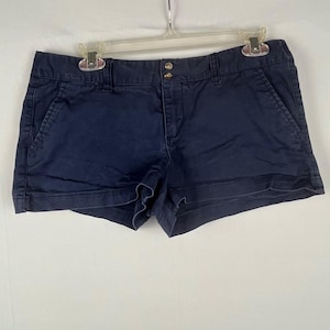 May include: Navy blue shorts with a button and zip fastening. The shorts have two front and two back pockets. The shorts are hanging on a clear plastic hanger.