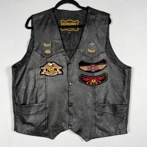 Könnte beinhalten: Schwarze Lederweste mit mehreren Aufnähern, darunter "RMC Harley Owners Group" und "HKG 2002". Die Weste hat zwei Vordertaschen, einen Knopfverschluss und ein "GENUINE"-Etikett. Eine klassische Bikerweste.