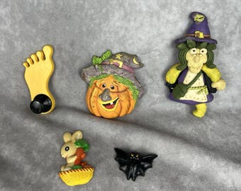 May include: A selection of Halloween-themed figurines. Includes a yellow foot with a black suction cup, a smiling pumpkin with a witch hat, a witch, a bunny with carrots in a basket, and a black bat.