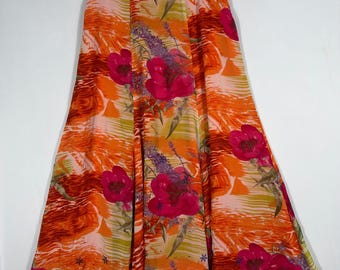 May include: A long, flowing skirt with a vibrant floral print. The skirt features large, bright pink flowers and purple accents against an orange and peach background. The skirt is hanging on a hanger.