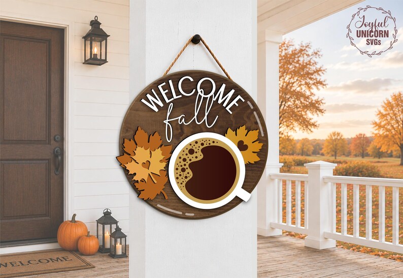 May include: A round wooden sign with the words "WELCOME fall" in white script. The sign features a coffee cup graphic and autumn leaves. The sign is hanging on a white wall, with pumpkins and lanterns in the background.