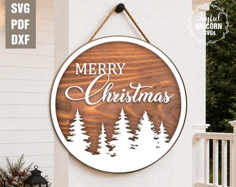 May include: A round wooden sign with a white border and a rope hanger. The sign features the words "MERRY Christmas" in white script above a white silhouette of pine trees. The background is a wood grain pattern.
