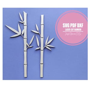 May include: Two laser-cut bamboo stalks with leaves, in a light color, are displayed against a blue background. The image includes text in a pink circle that reads "SVG PDF DXF LASER CUT BAMBOO Joyful Unicorn SVGs."