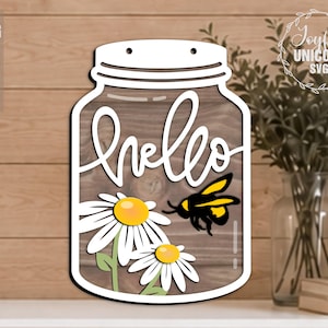 May include: A wooden jar-shaped sign with the word "hello" in cursive. The sign features daisies and a bee. The sign is white with a wooden background. The sign has two holes at the top for hanging.