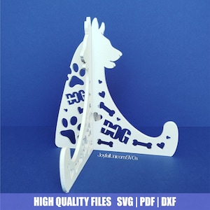 May include: A white, laser-cut dog-shaped stand with paw prints, hearts, and bone cutouts. The word "DOG" is cut out in two places. The stand is on a blue background. Text at the bottom reads "HIGH QUALITY FILES SVG | PDF | DXF".