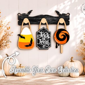 Puede incluir: Un estante de pared de madera negra con siluetas de murci&eacute;lagos que presenta tres decoraciones colgantes: una forma de caramelo de ma&iacute;z con murci&eacute;lagos, un letrero negro con texto blanco Trick or Treat y una forma de piruleta naranja y negra.