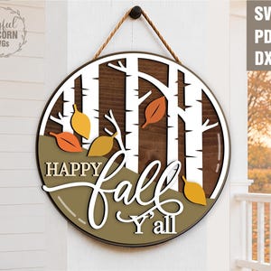 May include: A round wooden sign with a fall theme. The sign features the words "Happy Fall Y'all" in white script, with colorful leaves and a birch tree design. It is suspended by a brown rope.