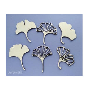 Puede incluir: Seis recortes de hojas de ginkgo de madera en varios diseños, incluyendo estilos sólidos y calados. Las hojas son de color claro y están dispuestas sobre un fondo azul claro. La imagen incluye el texto "Joyful Unicorn SVG".