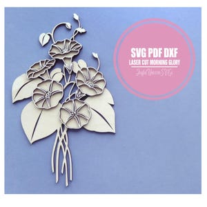 May include: A wooden laser-cut design of morning glory flowers and leaves. The flowers have detailed petal patterns, and the leaves are large and rounded. The design includes the text "SVG PDF DXF LASER CUT MORNING GLORY" and "Joyful Unicorn SVGs" in a pink circle.
