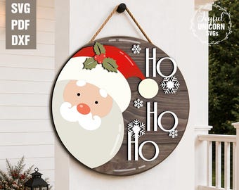 May include: A round wooden Christmas sign featuring Santa Claus with a red hat and white beard. The sign says "Ho Ho Ho" with snowflake accents. The sign is hanging by a rope.