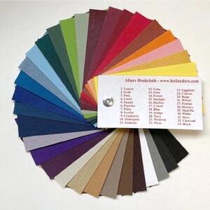 May include: A color chart of 33 different fabric swatches, arranged in a fan shape. The swatches are labeled with numbers and names, such as "Lemon", "Gold", "Pink", "Coral", "Sunset", "Paprika", "Flare", "Scarlet", "Cranberry", "Mahogany", "Seafoam", "Lime", "Fern", "Forest", "Skylight", "Harbor", "Cobalt", "Blue", "Indigo", "Navy", "Wisteria", "Plum", "Eggplant", "Canvas", "Beige", "Wheat", "Praline", "Hickory", "Mud Pie", "White", "Dove", "Charcoal", "Black". The chart is labeled "Allure Bookcloth - www.hollanders.com".