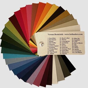 May include: A color chart of 32 fabric swatches, arranged in a fan shape. The swatches are labeled with numbers and names, such as "Snowflake", "Parchment", "Bisque", "Hot Toffee", "Espresso", "Lemon Appeal", "Pumpkin", "Orange Blast", "Sedona", "Pink Punch", "Ablaze", "Rock'n Red", "Merlot", "Lemongrass", "Artichoke", "Olive", "Forest", "Emerald", "Summer Pool", "Steel Blue", "Blueberry", "Marine", "Blue Jay", "Sapphire", "Lilac", "Berry Bloom", "Fig", "Plum", "White", "Smoke", "Gunmetal", and "Coal Black". Verona Bookcloth - www.hollanders.com is printed on the chart.