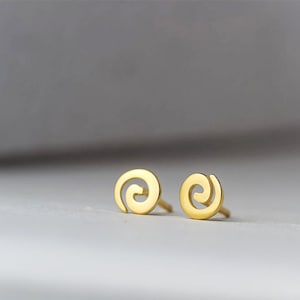May include: A pair of gold-toned spiral stud earrings. The earrings are small and delicate, and they have a simple, modern design.