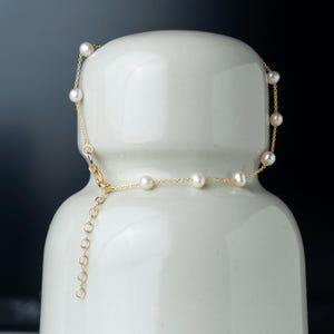 Può includere: Una delicata collana a catena dorata con piccole perle bianche. La collana ha una chiusura a moschettone e un piccolo estensore a catena.