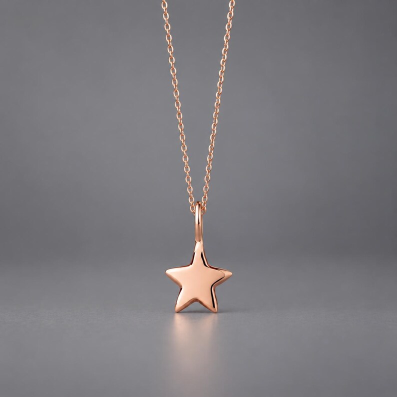 May include: A rose gold-toned necklace featuring a delicate chain and a smooth, five-pointed star pendant. The star charm is suspended from a simple jump ring, creating a clean and polished look with a warm metallic finish throughout the piece.
