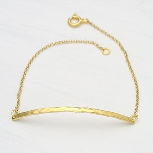 May include: A gold chain bracelet with a hammered gold bar pendant.