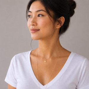 May include: A delicate gold-toned layered necklace featuring a small, five-pointed star charm on the shorter chain. The necklace consists of two thin, minimalist chains of varying lengths that rest against the collarbone and chest area.