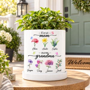 May include: A white ceramic planter containing a green plant, featuring the text first mom now grandma with watercolour illustrations of seven flowers and names: Olivia, Hunter, Sophia, Grayson, Daisy, Jasmine, and Jonah, accented by small butterflies.