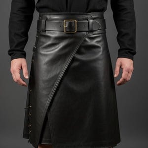 K&ouml;nnte beinhalten: Schwarzer Lederkilt mit Wickeldesign und G&uuml;rtel mit rechteckiger Schnalle. Der Kilt hat dekorative N&auml;hte und einen Seitenschlitz. Das Model tr&auml;gt ein schwarzes Langarmshirt.