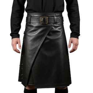 K&ouml;nnte beinhalten: Schwarzer Lederkilt mit Wickeldesign und G&uuml;rtel mit quadratischer Schnalle. Der Kilt hat dekorative N&auml;hte an der Seite. Getragen mit einem schwarzen Langarmshirt.