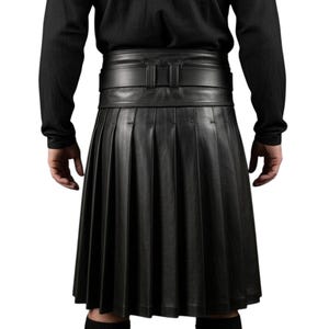 K&ouml;nnte beinhalten: Ein schwarzer Lederkilt mit tiefen Falten und einem breiten G&uuml;rtel mit Schnalle. Der Kilt wird mit einem schwarzen Langarmshirt getragen. Das Bild zeigt die R&uuml;ckansicht des Kilts.