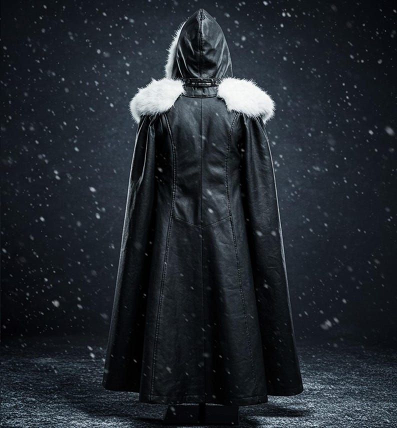 May include: A black leather hooded cape with a white fur collar. The cape is long and flowing, and the hood is pulled up over the head. The cape is worn by a person standing in a snowy setting.