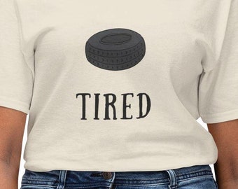 Op de afbeelding: Een lichtbeige t-shirt met een zwarte bandenprint en het woord "TIRED" eronder gedrukt.