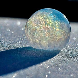 May include: A large, iridescent soap bubble with intricate patterns frozen on a sparkling, white surface.