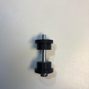 May include: A black rubber and metal component with a threaded top and a hexagonal nut at the bottom. The component has a silver metal rod and is designed for mechanical use.