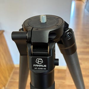 May include: A black tripod with three legs, featuring a central mounting plate with a threaded screw. The tripod has the brand name "FANUE" and model number "HT-3240-45" printed on it. The legs have a textured pattern.