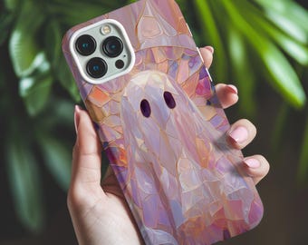 May include: A smartphone case featuring a ghost design. The case has a mosaic-like pattern in shades of pink, purple, and gold. The ghost has two dark oval eyes. The phone case is held in a hand.