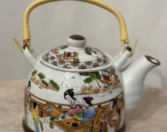 May include: White porcelain teapot with a bamboo handle and a painted scene of people in a landscape. The teapot has a brown rim and a brown base.