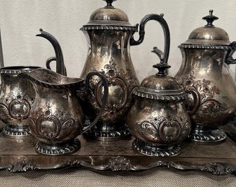 May include: A silver tea set with ornate floral designs on a silver tray. The set includes a teapot, creamer, sugar bowl, and two cups.