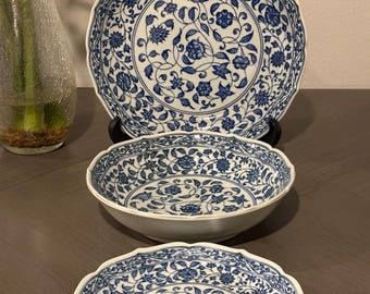 May include: A set of three white ceramic bowls with a blue floral pattern. The bowls are different sizes and have a scalloped edge.