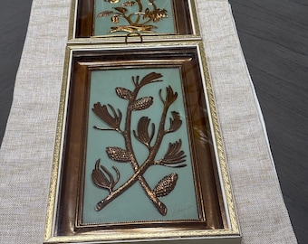 May include: Two rectangular wall plaques featuring metallic copper-toned botanical reliefs set against a pale mint green background. Each plaque is encased in a dark brown frame with a gold-toned inner border and a white outer edge, topped with a small metal loop.