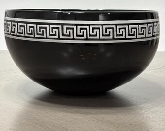 May include: A glossy black ceramic bowl featuring a wide, horizontal band around the upper exterior. This band displays a repeating white Greek key pattern, also known as a meander design, which contrasts sharply against the dark, reflective surface.