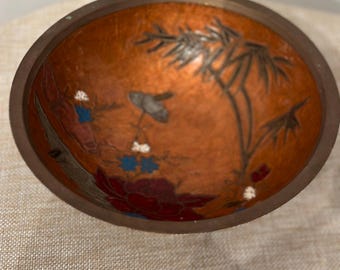 May include: A small, round, brown bowl with a painted design of flowers and bamboo. The bowl has a glossy finish and is decorated with red, blue, and white paint.
