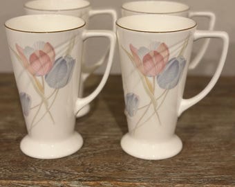 May include: Set of four white ceramic mugs with gold trim and a floral design featuring pink, blue, and green tulips.