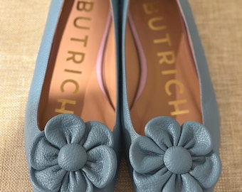 May include: A pair of blue leather flats with a flower detail on the toe. The shoes are labeled "Butrich" on the inside.