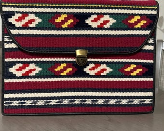 May include: A red, black, white, green, and yellow patterned briefcase with a black leather handle and a brass clasp.