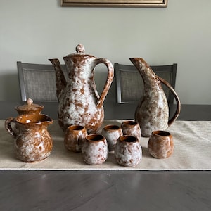 May include: A set of brown and white ceramic pottery, including a teapot, creamer, sugar bowl, and six cups. The pottery has a speckled glaze.