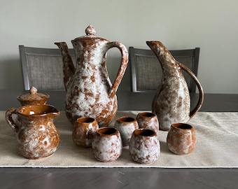 May include: A set of brown and white ceramic pottery, including a teapot, creamer, sugar bowl, and six cups. The pottery has a speckled glaze.