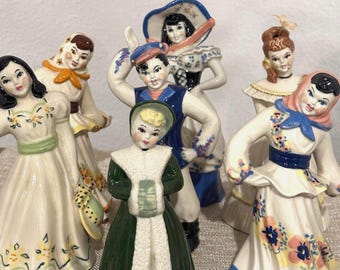 May include: Set of six vintage porcelain figurines depicting people in traditional clothing. The figurines are painted in various colors, including blue, green, yellow, and pink. They are all wearing hats and have smiling faces.