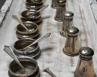 May include: An arrangement of antique silver salt cellars with small spoons and matching salt shakers. The salt cellars are round with a small spoon inside. The salt shakers are cone-shaped with a perforated top.