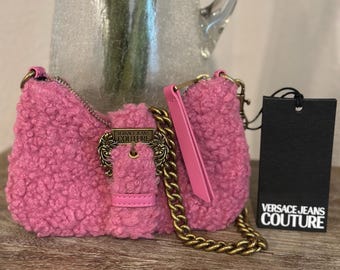 May include: A pink, textured shoulder bag with a gold chain strap and a decorative buckle. The bag has a matching pink handle and a black tag with the "VERSACE JEANS COUTURE" logo.