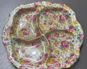 May include: A floral-patterned serving dish with three compartments. The dish features a scalloped edge and is decorated with a pattern of pink, yellow, and blue flowers on a cream background. The dish is likely made of ceramic.