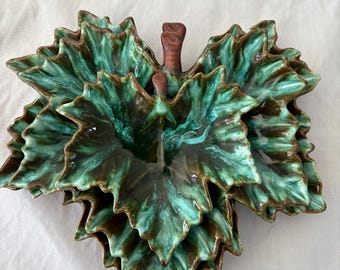 May include: A ceramic leaf-shaped serving dish with a layered design. The dish features a glossy, mottled green and brown glaze, with a textured surface. The dish has a stem-like handle and is suitable for serving appetizers or snacks.
