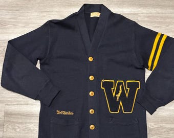 May include: A navy blue cardigan with a large yellow felt "W" on the front. The cardigan has two pockets and yellow stripes on the sleeves. The text "Golf Bankers" is embroidered on the left pocket.